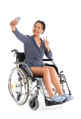 Asian woman in wheelchair taking selfie on white background