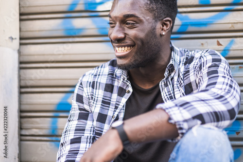 Fotografía Handsome cheerful beautiful young black man african american smiling and having fun while sit and relax in the city with urban background