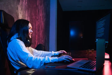 Cheerful young woman freelancer in casual wear typing programming code work on modern laptop computer at home. Positive student updating software on netbook