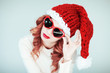 Santas little helper. Beautiful happy young woman with a santa claus hat, perfect make up, red lipstick, and heart shape sun glasses, silly and funny mood 