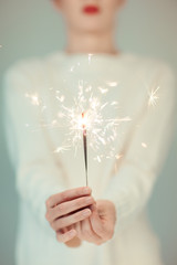 Beautiful woman hands holding sparkler lights, cozy, bright winter sweater, can be used as background 