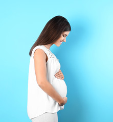 Wall Mural - Happy pregnant woman posing on color background. Space for text