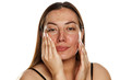 beautiful middle-aged woman applying moisturizer on her face on white background