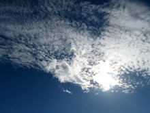 Dark Blue Sky With White Cirrus Clouds, Sun Is Shining Through The Cloud. Beautiful Weather Background