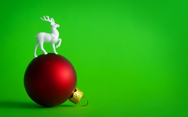 white reindeer on red christmas bauble decoration on green background. holiday concept.