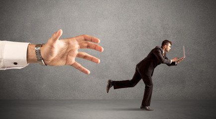 Wall Mural - Young miniature businessman running from a big hand with light grey background