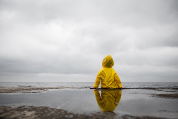 Wall Mural - Rainy clouds. Child in a yellow raincoat.