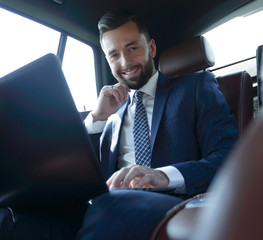 Wall Mural - Caucasian male business executive travelling by a car and working on laptop computer.