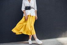 Horizontal Cropped Body Image Of Beautiful Slim Woman In Beautiful Yellow Skirt. Caucasian Female Fashion Model Standing Over Gray Wall Background Outdoor With Copy Space.