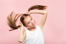 Happy Joyful Smiling Adolescent Girl Making Pig Tails From Her Hair. Relaxed Carefree Lifestyle And Childish Behavior. Young Cute Brown Haired Kid Portrait On Pink Background.