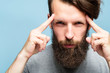 © golubovy - mind games and brain power. mentalist and cognitive skills concept. man concentrating and holding index fingers on temples. young bearded guy portrait on blue background.
