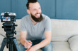 © golubovy - vlogging and freelance job concept. bearded man shooting video of himself using camera on tripod and creating content for social media.