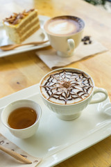 hot coffee late in white glass on wooden table, blurred cake and wooden spoon,