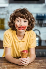 Wall Mural - adorable boy with ice cream on face holding delicious ice cream cone and looking at camera