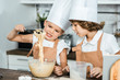 cute little children in aprons and chef hats preparing dough for tasty cookies together