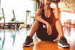 Sport woman relax resting after workout or exercise in fitness gym. Sitting and drinking protein shake or drinking water on floor. Strength training and Bodybuilder muscle theme. Warm and cool tone