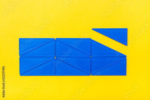 Fotografie, Obraz Blue plastic triangles are laid out in straight rows in a rectangle on a yellow background