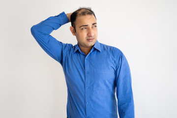 Wall Mural - Pensive Indian man scratching back of head and looking away. Young guy thinking. Confusion concept. Isolated front view on white background.