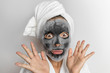 Face mask bubble foam facial funny woman at beauty spa looking shocked or surprised, scary chemicals in beauty products. Asian girl wearing bath towel on hair.