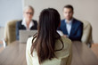 © fizkes - Businesswoman and businessman HR manager interviewing woman. Candidate female sitting her back to camera, focus on her, close up rear view, interviewers on background. Human resources, hiring concept