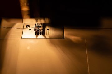 Wall Mural - Modern compact electric sewing machine in the evening. View of needle and thread. Illumination from the built-in incandescent lamp. Sewing machine is used to stitch fabric and other materials together