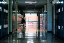 Straight View Of Darkly Lit Hallway With Bright Light At End And Lockers Covering The Walls On Either Side 