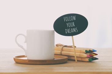 Wall Mural - sign with text: FOLLOW YOUR DREAMS next to cup of coffee over wooden table.
