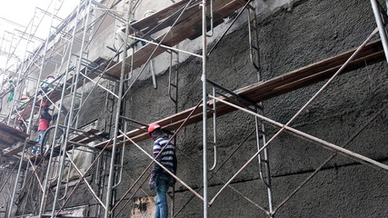 Wall Mural - Brick wall plastered by construction workers using the cement plaster. Scaffolding used as temporary staging to work at height. Wearing appropriate safety gear to prevent bad happen.  