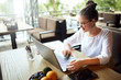 © artiemedvedev - Young mixed race woman working with laptop in cafe at tropical location. Asian caucasian female studying using internet. Business woman doing social marketing work and shopping. Telecommuting concept.