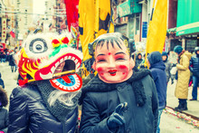 Two People Wearing Traditional Chinese Masks, Big Head Doll And Lion, Walking On Street In Chinatown, Downtown Of Manhattan, New York City, Celebrating Chinese New Year. Many People On Background. 