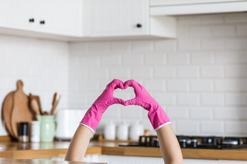 heart made of pink protective gloves on white kitchen background.. woman hands wearing protective gl
