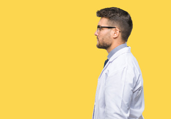 Young handsome man wearing doctor, scientis coat over isolated background looking to side, relax profile pose with natural face with confident smile.