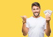 © Krakenimages.com - Young handsome man holding stack of dollars over isolated background pointing and showing with thumb up to the side with happy face smiling
