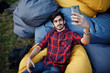 © AS Photo Family - Young indian student man at checkered shirt and jeans sitting and relax at outdoor pillows and making selfie.