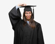 © Krakenimages.com - Young hispanic woman wearing graduated cap and uniform confuse and wonder about question. Uncertain with doubt, thinking with hand on head. Pensive concept.