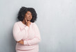 © Krakenimages.com - Young african american plus size woman over grey grunge wall wearing winter sweater with hand on chin thinking about question, pensive expression. Smiling with thoughtful face. Doubt concept.