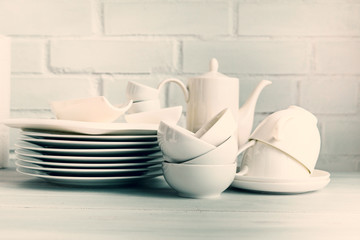 Wall Mural - White porcelain  dishware stacked on a wooden table against white brick background. Concept of restaurant, cooking and service.