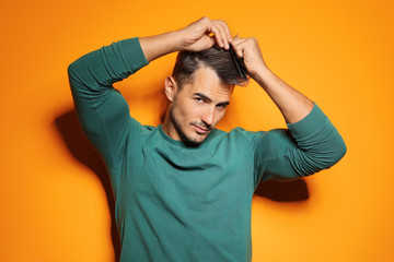 Wall Mural - Young man with comb posing on color background. Trendy hairstyle