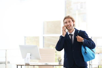 Young handsome businessman holding fitness bag in office. Space for text