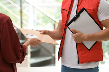 Wall Mural - Woman receiving envelope from delivery service courier indoors