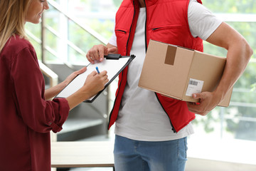 Wall Mural - Young woman signing papers for delivered parcel indoors. Courier service