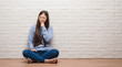 © Krakenimages.com - Young Chinese woman sitting on the floor over brick wall looking confident at the camera with smile with crossed arms and hand raised on chin. Thinking positive.