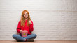 © Krakenimages.com - Young redhead woman sitting over brick wall eating popcorn happy with big smile doing ok sign, thumb up with fingers, excellent sign