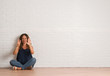 © Krakenimages.com - Middle age hispanic woman sitting on the floor over white brick wall showing and pointing up with fingers number eight while smiling confident and happy.