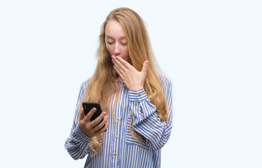 Sticker - Blonde teenager woman using smartphone cover mouth with hand shocked with shame for mistake, expression of fear, scared in silence, secret concept