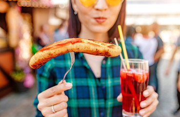 Young happy asian traveler woman eating fried sausage and drinks mug of beer at the fair market square in Germany, beer and food festival concept