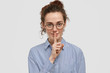 © WHstudio Leushin N - People, secrecy and conspiracy concept. Mute youngster with freckles, curly hair, holds fore finger over lips, demonstrates secret gesture, dressed in striped shirt, stands against white background