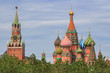 Domes of St. Basil's Cathedral on Red square with Spasskaya tower of Moscow Kremlin against green trees and cloudy sky at summer day