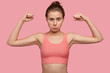Self detrermined fit woman with sporty body, shows muscles, wears casual top, purses lips, ready for workout and physical training, isolated over pink background. People and motivation concept