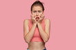 Stressful active young European sportswoman has nnervous expression, worries before important competition, dressed in casual top, poses alone against pink background. Sport and lifestyle concept